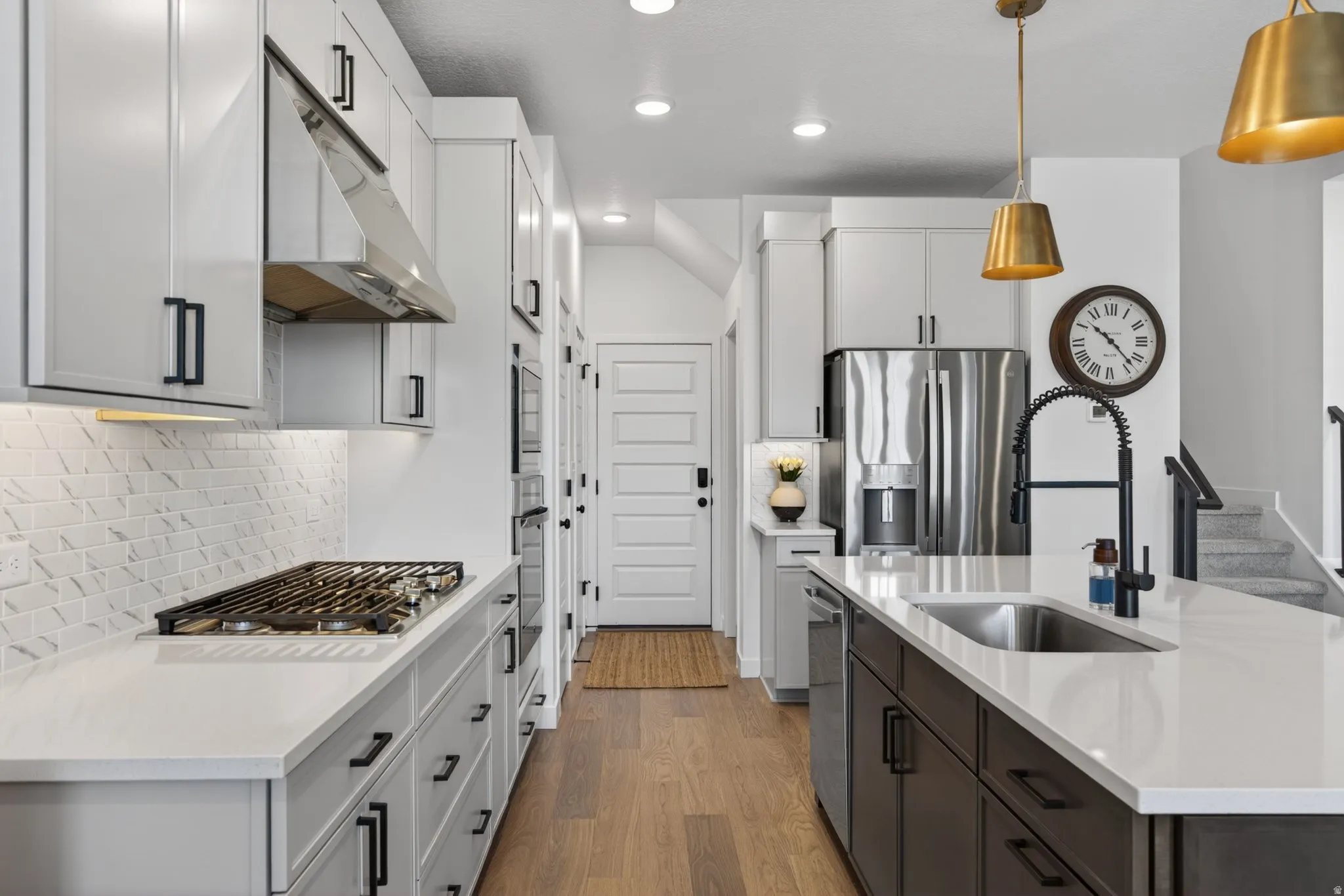 Gourmet kitchen featuring a gas range, stainless steel appliances, white cabinetry, dark island cabinetry, and wood-finish flooring