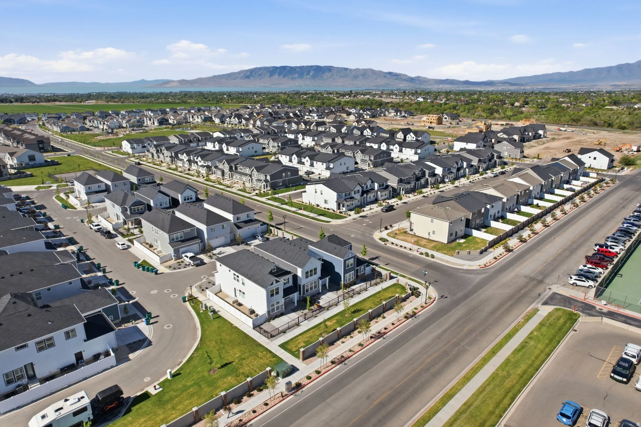 Expansive residential development featuring modern homes with dark roofs, manicured green spaces, paved streets, and mountainous terrain in the distance