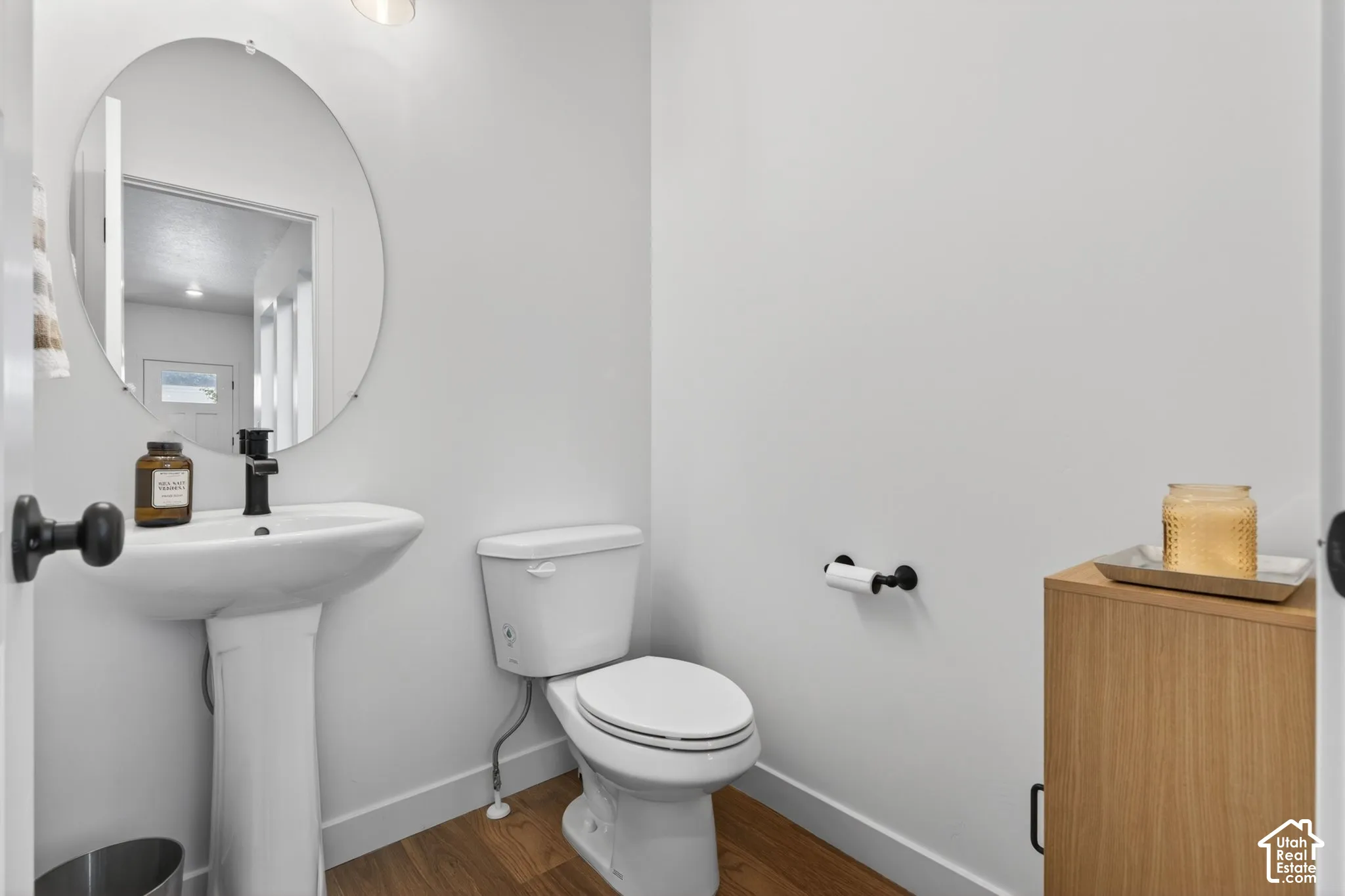 Pedestal sink with a matte black faucet, complemented by a circular wall-mounted mirror
