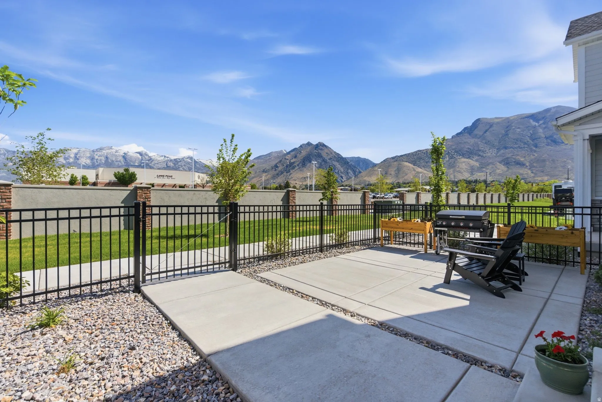 Expansive concrete patio bordered by decorative gravel, featuring a black metal fence and a manicured lawn