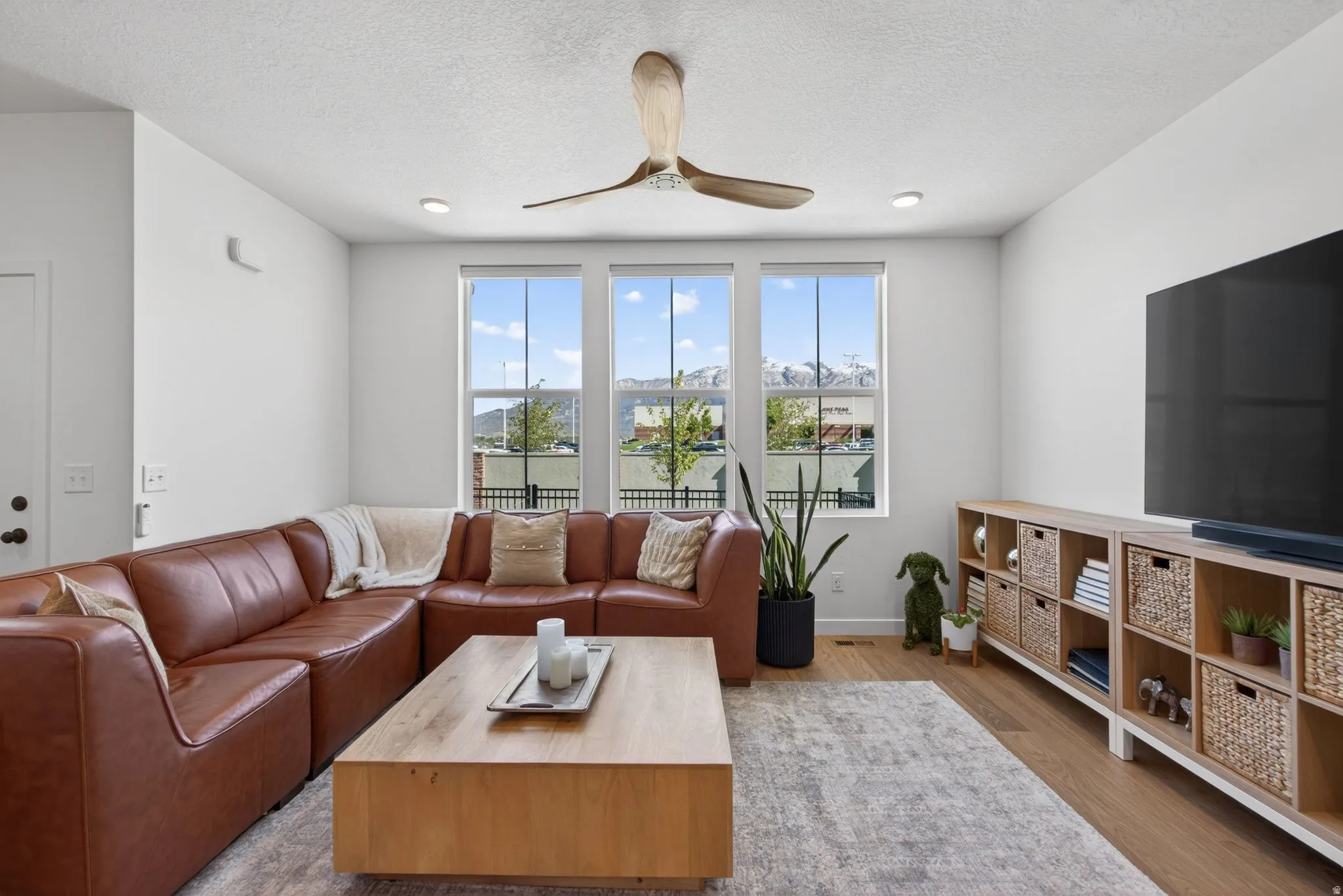 Lounge area featuring three large windows, a ceiling fan with wooden blades, recessed lighting, and wood-finish flooring