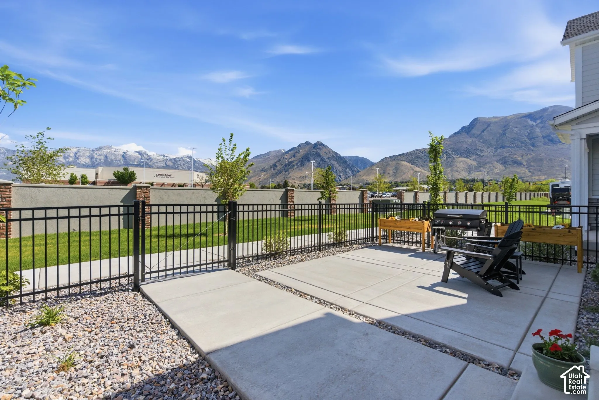 Expansive concrete patio bordered by decorative gravel, featuring a black metal fence and a manicured lawn