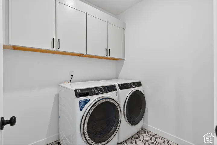 Laundry area featuring white cabinetry with black hardware, a wood-finish shelf, and hexagonal floor tiling