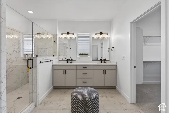 Contemporary bathroom featuring a spacious glass-enclosed shower with marble-look tile, a dual vanity with light gray cabinetry and white countertops, dual framed mirrors, and stylish wall-mounted light fixtures