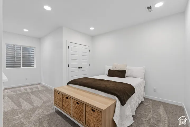 Spacious room featuring neutral carpeting, a double-door closet with black hardware, a window with horizontal blinds, and recessed lighting