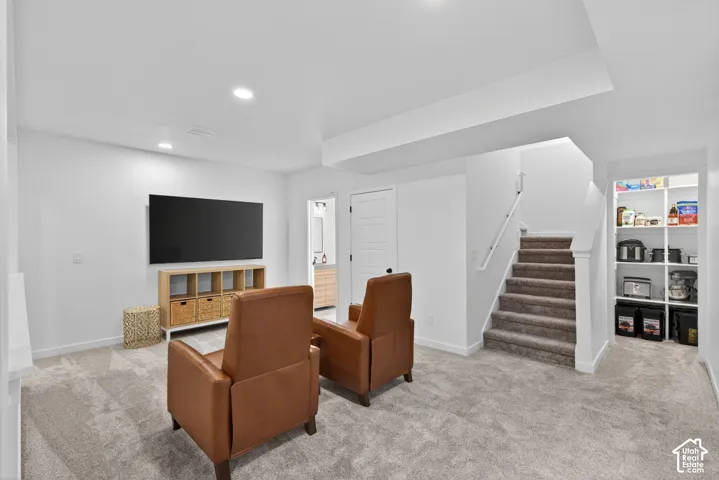 Carpeted recreation room featuring recessed lighting, a built-in shelving unit, and a carpeted staircase with a white handrail