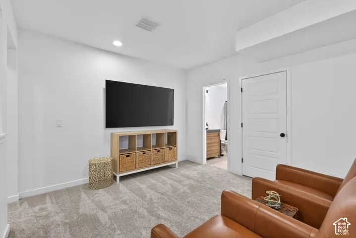 Spacious carpeted room featuring a wall-mounted display, recessed lighting, and a white five-panel interior door