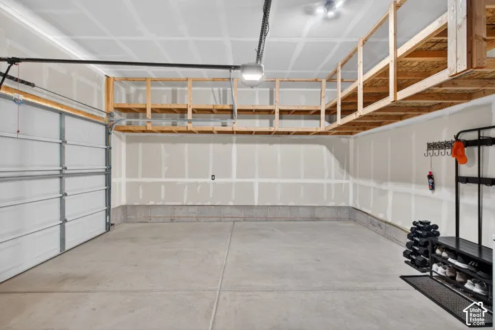 Spacious garage featuring a concrete floor, overhead wood-frame storage shelving, and a white paneled garage door