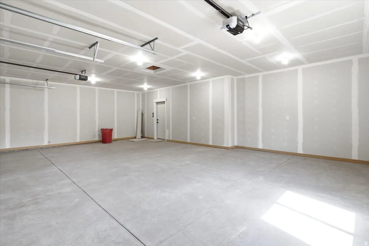 Spacious garage featuring a concrete floor, high ceilings, multiple overhead light fixtures, and an automatic garage door opener system