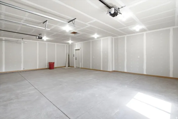 Spacious garage featuring a concrete floor, high ceilings, multiple overhead light fixtures, and an automatic garage door opener system