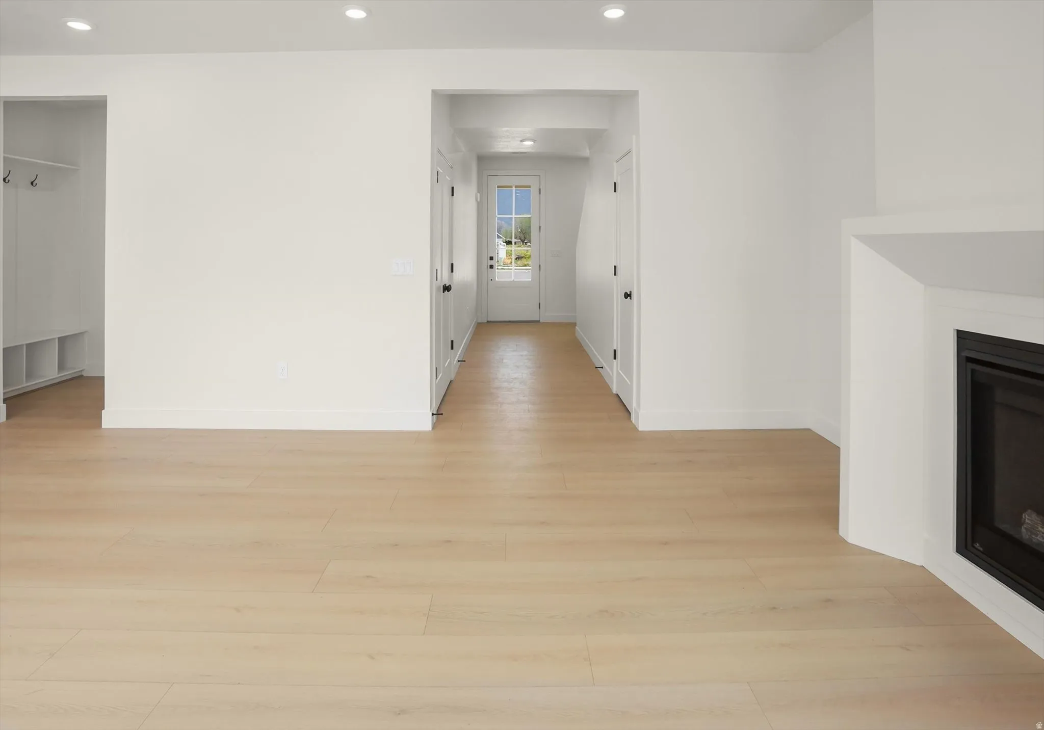 Spacious interior featuring light wood-finish flooring, recessed lighting, a fireplace with a white mantel, and a dedicated mudroom area with built-in storage and coat hooks
