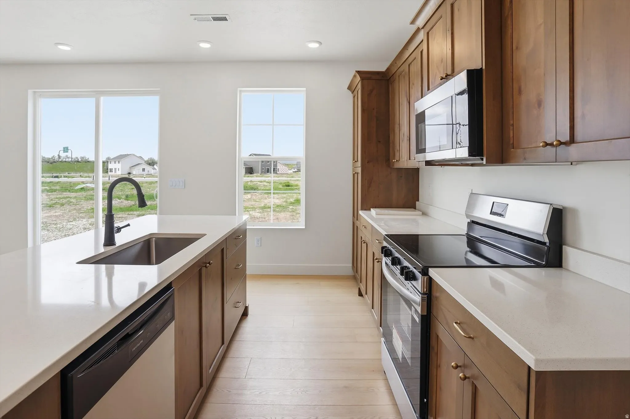 Kitchen featuring light wood-finish flooring, white countertops, wood cabinetry, stainless steel appliances, and a kitchen island with an undermount sink and matte black faucet