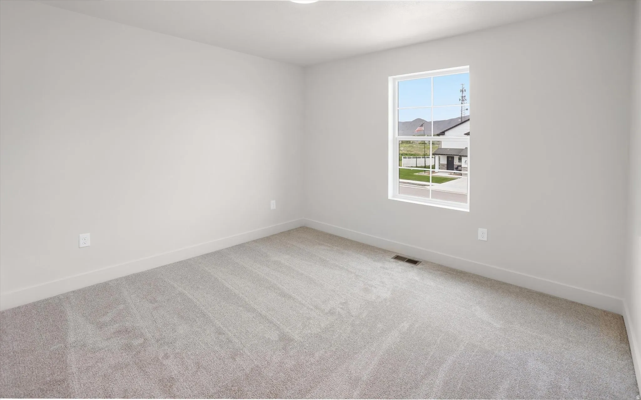 Neutral tone walls with soft gray carpet flooring, white trim, and a window providing natural light