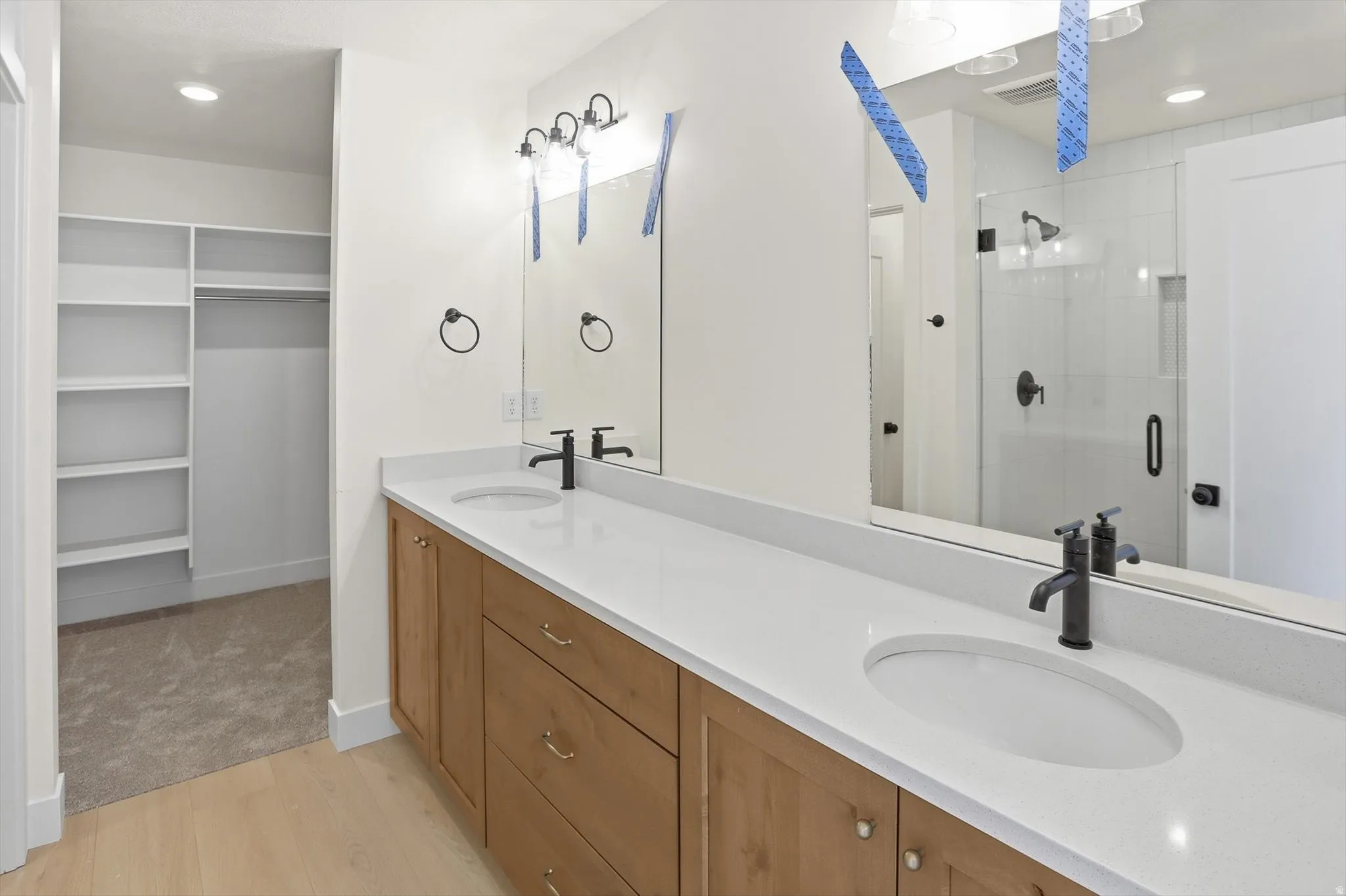 Spacious bathroom featuring a dual vanity with light wood cabinetry, white countertops, and matte black fixtures