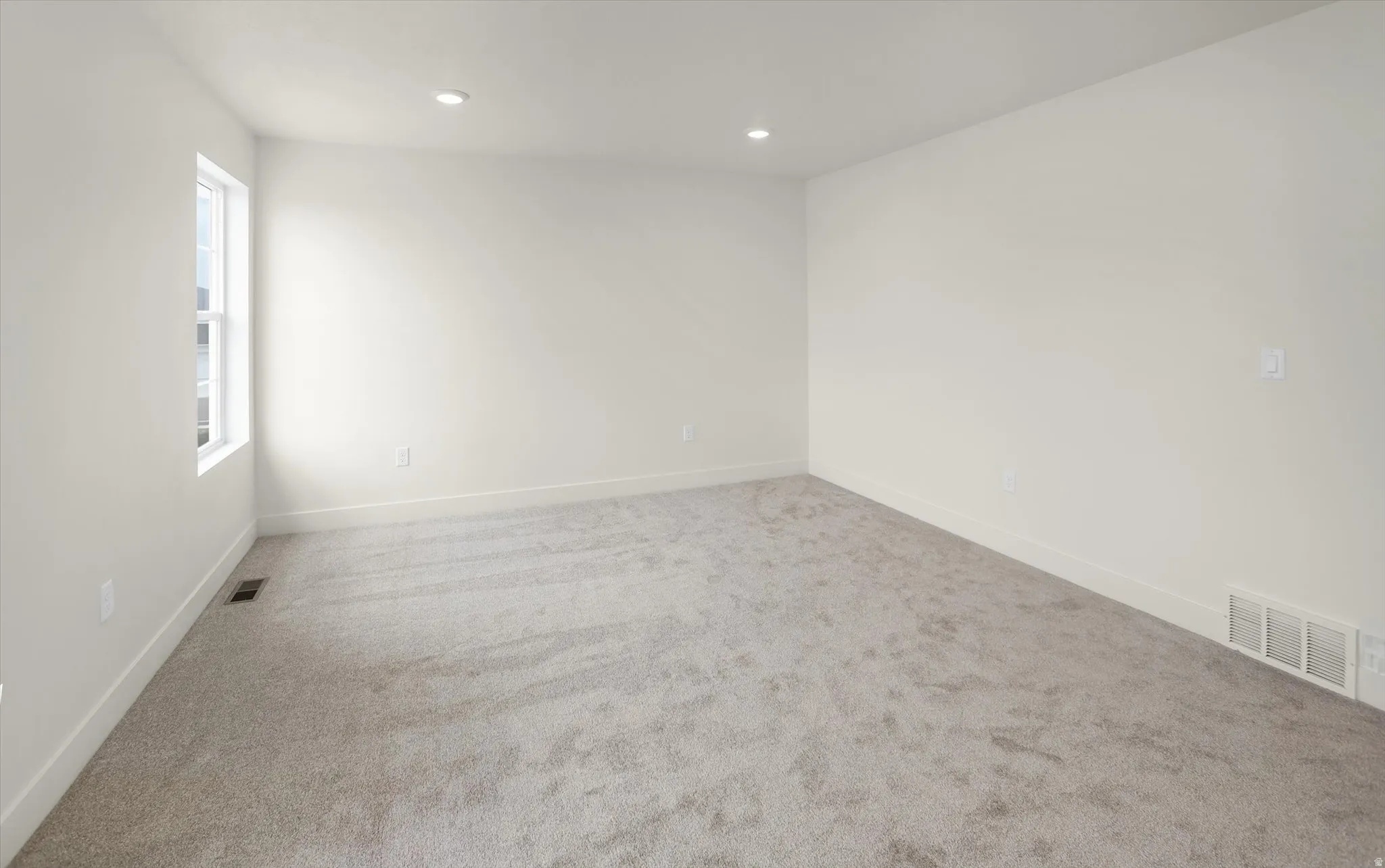 Spacious room featuring light gray carpeting, recessed lighting, white walls, and a single window with white trim