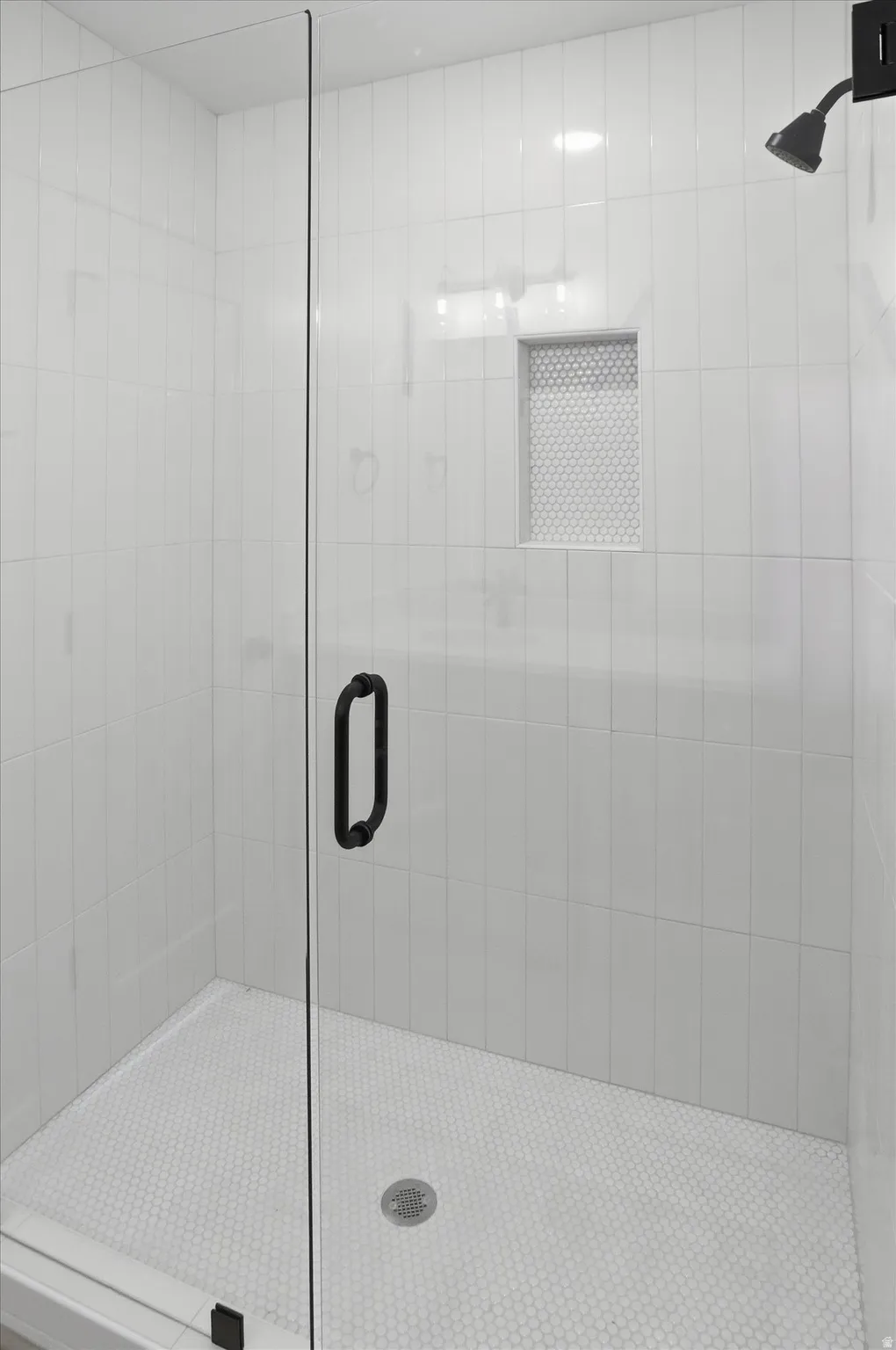 Walk-in shower featuring a frameless glass enclosure with matte black hardware, white vertical subway tile walls, a built-in shower niche with honeycomb tile, and a honeycomb tile shower floor