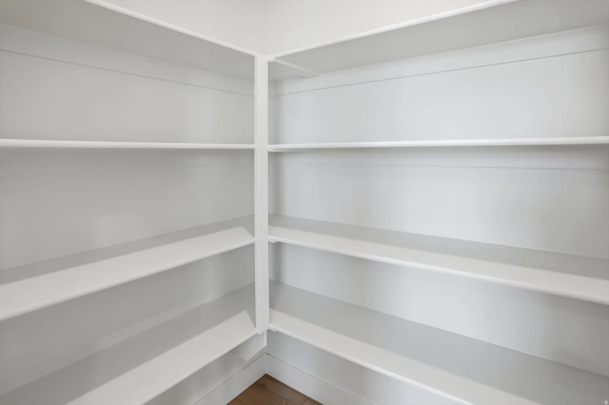 Built-in corner pantry shelving with white painted finishes and wood-finish flooring