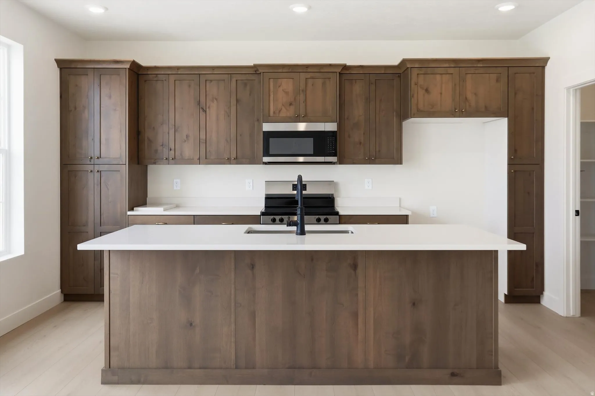 Modern kitchen featuring an island with an undermount sink, dark wood-finish cabinetry, light countertops, stainless steel appliances, and wood-finish flooring