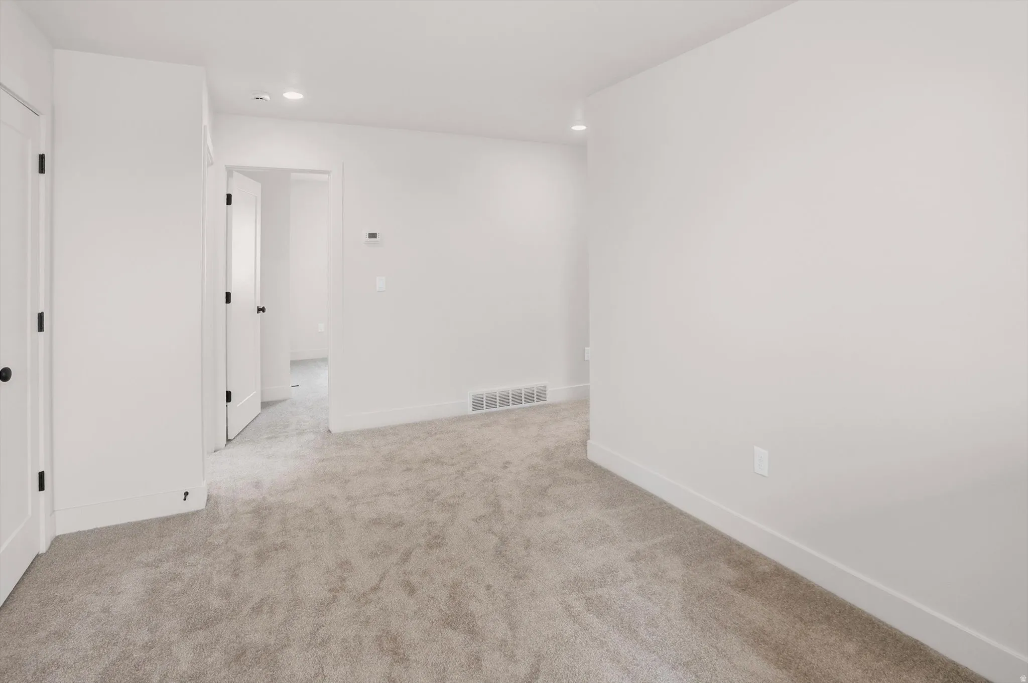 Spacious interior room featuring light gray carpet flooring and white painted walls