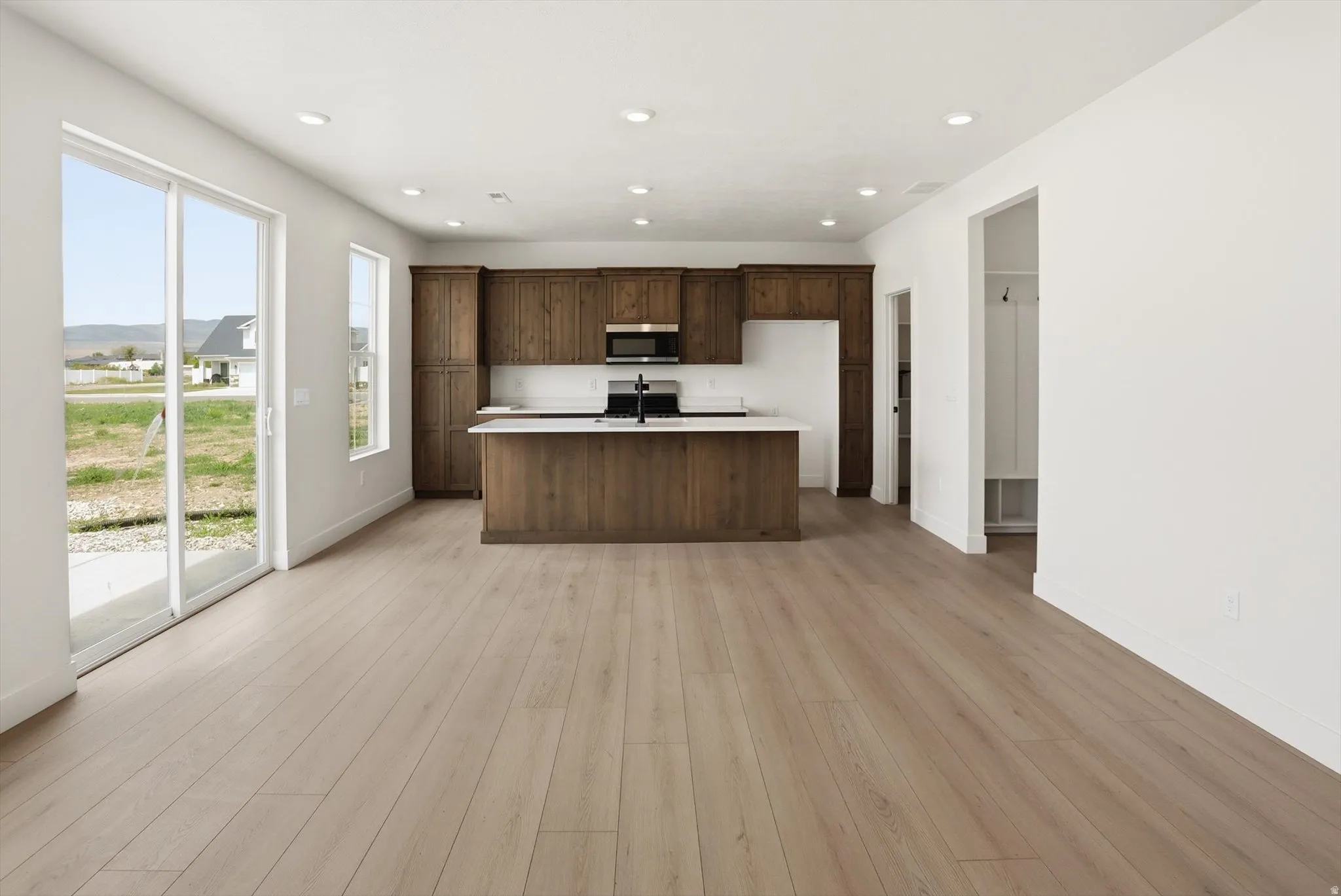 Open-concept living area with wood-finish flooring, a kitchen featuring dark wood cabinetry, and a central island with a white countertop