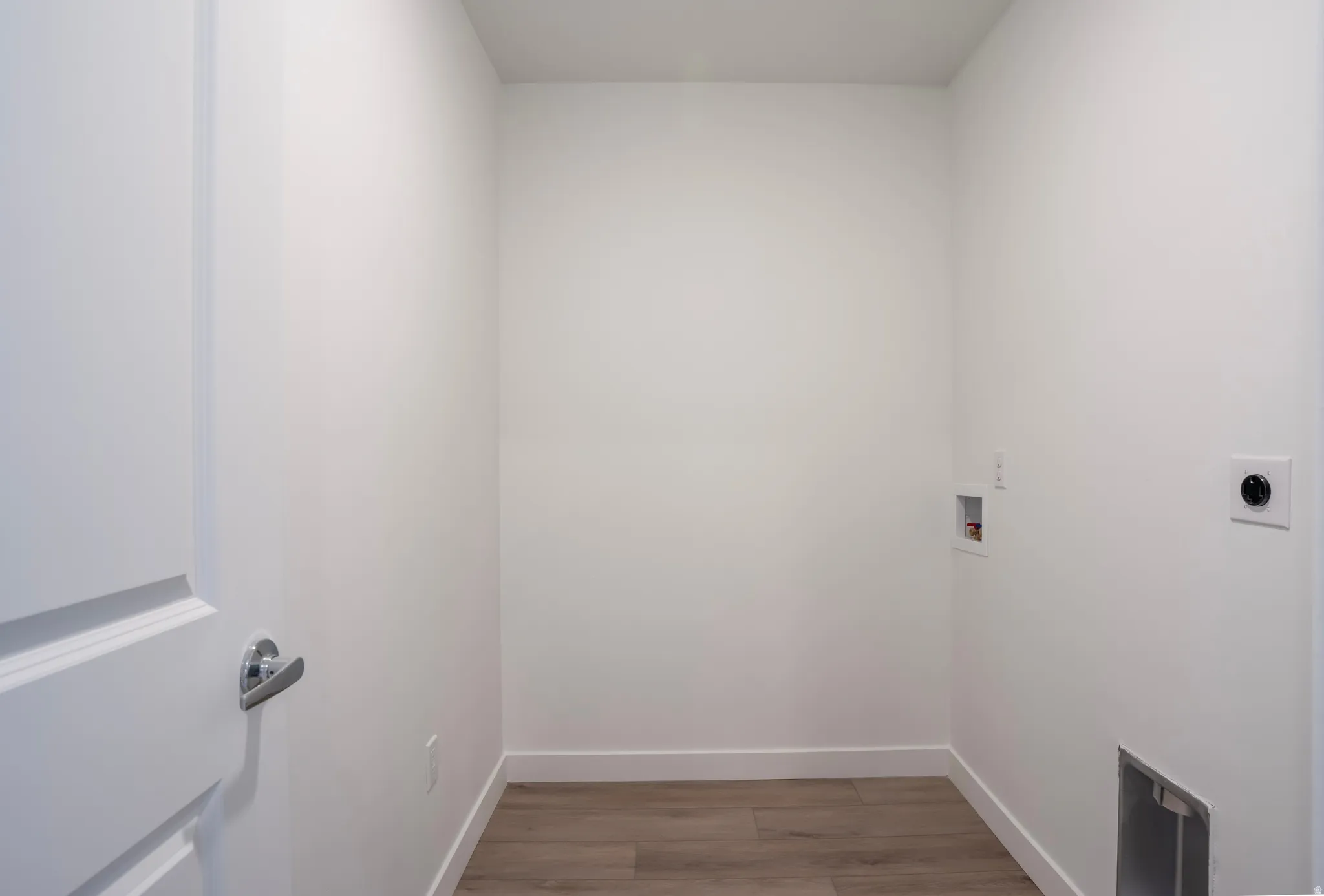 Dedicated laundry area featuring wood-finish flooring, white walls, and essential utility hookups