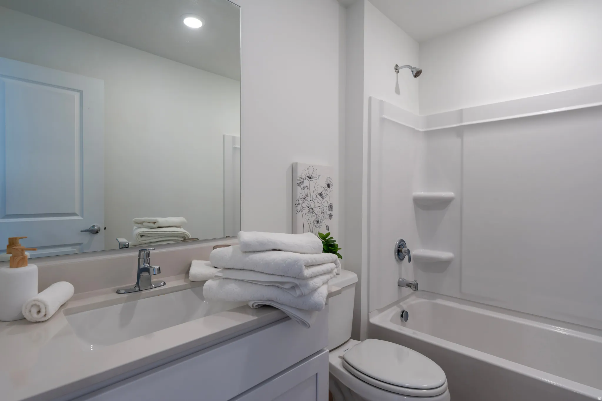 Full bathroom featuring a single vanity with an integrated sink, a rectangular mirror, a toilet, and a combined bathtub and shower with a chrome fixture
