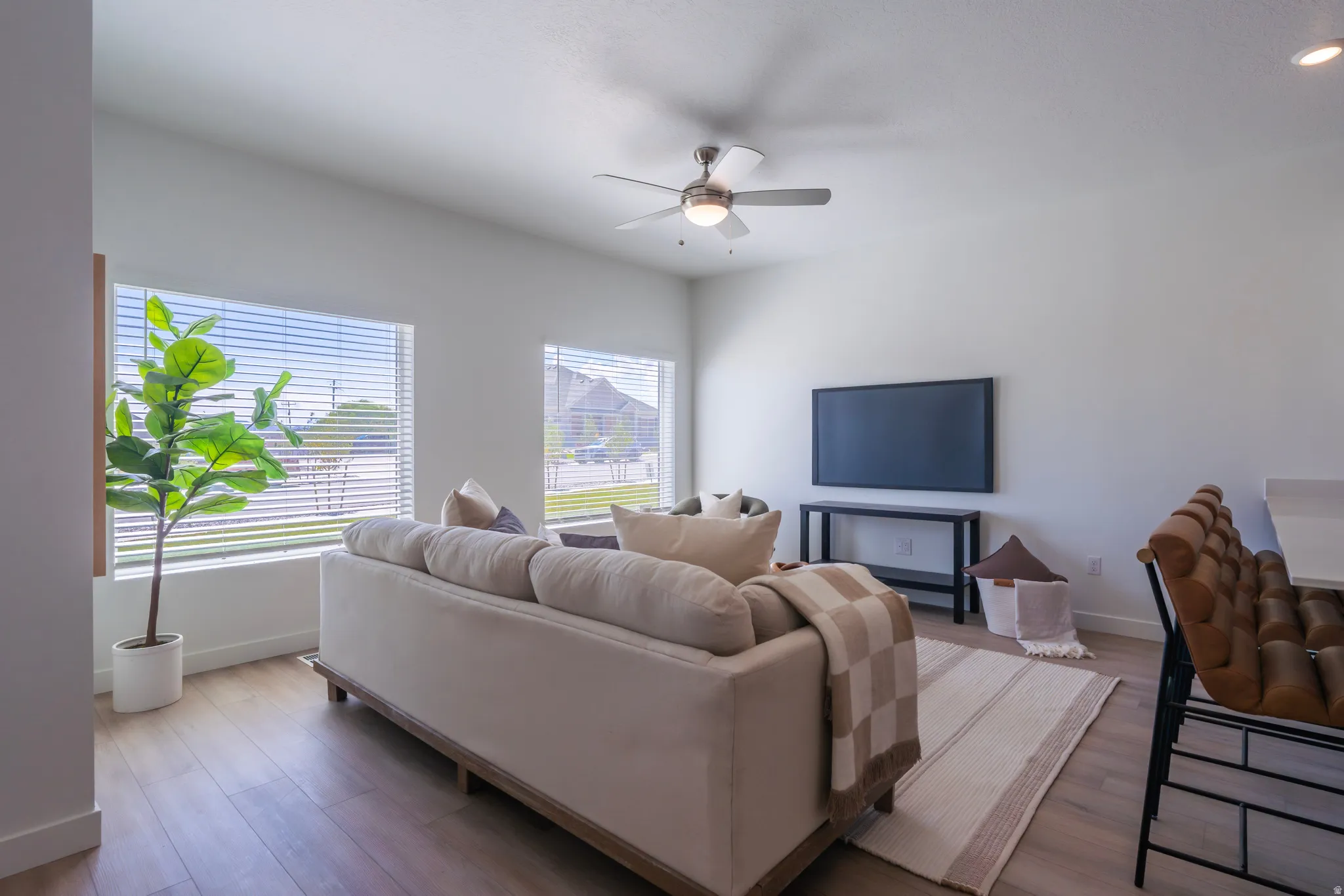 High ceilings featuring a ceiling fan, wood-finish flooring, multiple windows with blinds, and white walls