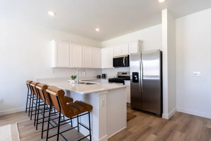 Contemporary kitchen featuring white cabinetry, light-toned countertops, stainless steel appliances, a kitchen island with an integrated sink, and wood-finish flooring
