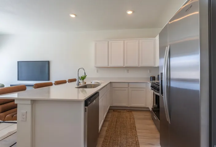Contemporary kitchen featuring white cabinetry, light-toned countertops, stainless steel appliances, and wood-finish flooring