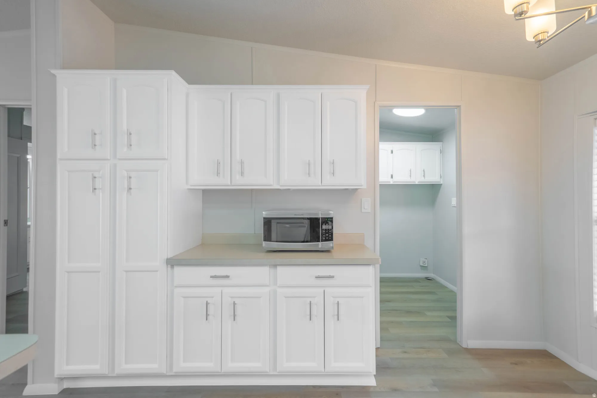 Kitchen featuring white shaker-style cabinetry, a light-toned countertop, and wood-finish flooring