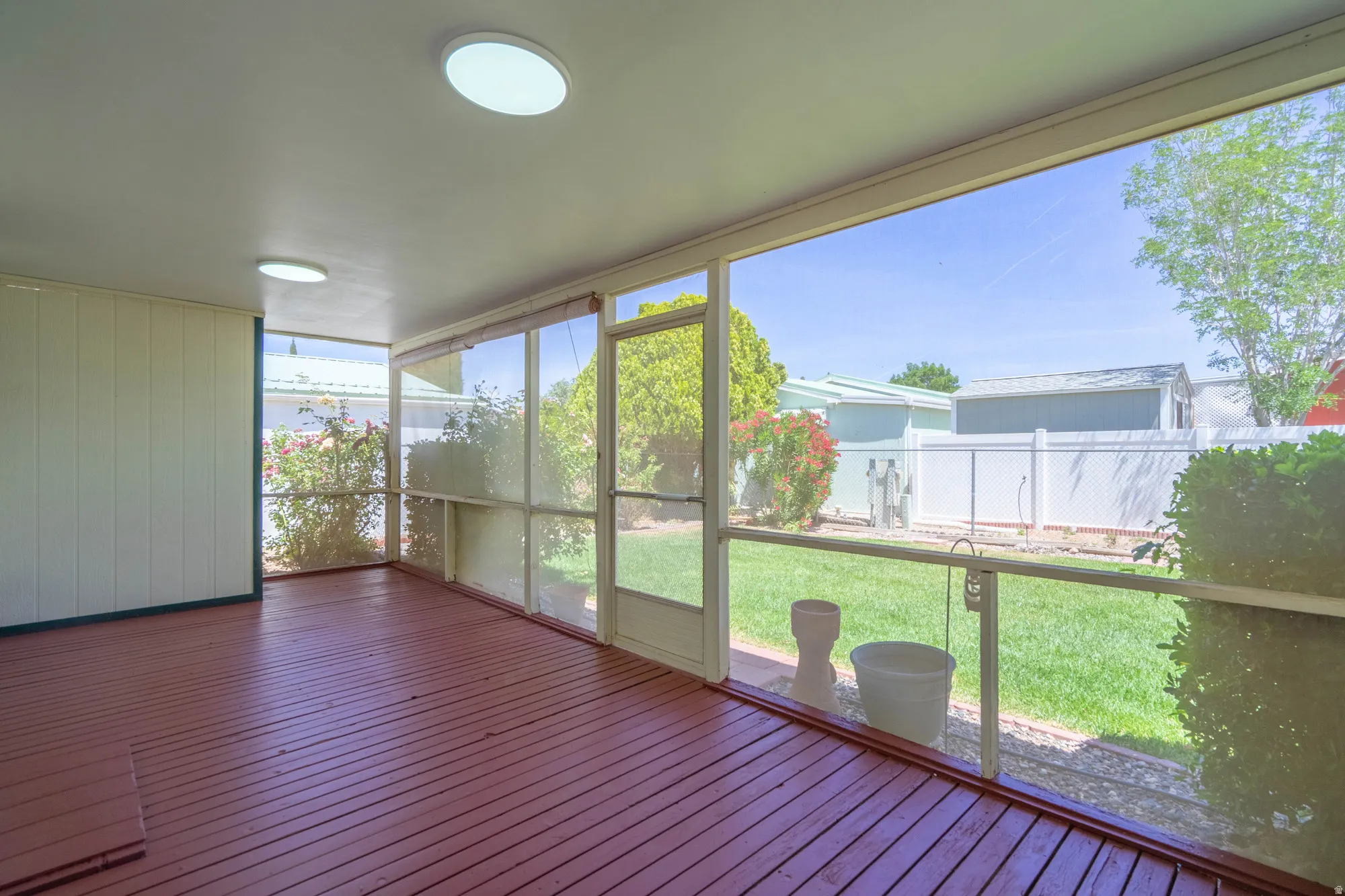 Screened porch featuring a wood-finish floor, white paneled walls, and two ceiling-mounted light fixtures