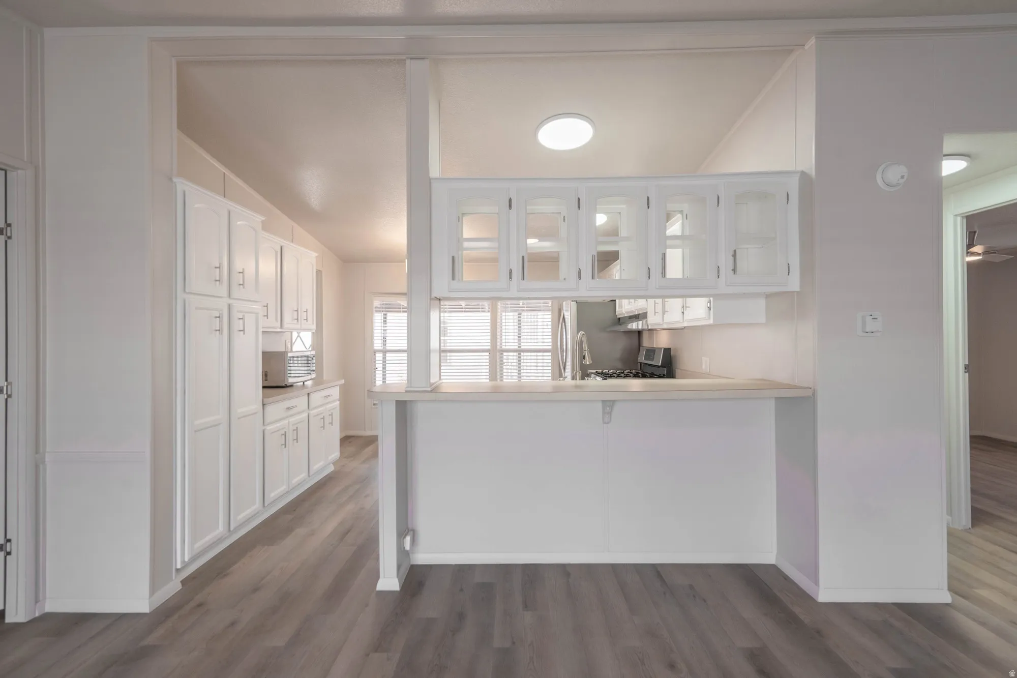 Kitchen area featuring wood-finish flooring, white cabinetry, a built-in breakfast bar, and recessed lighting