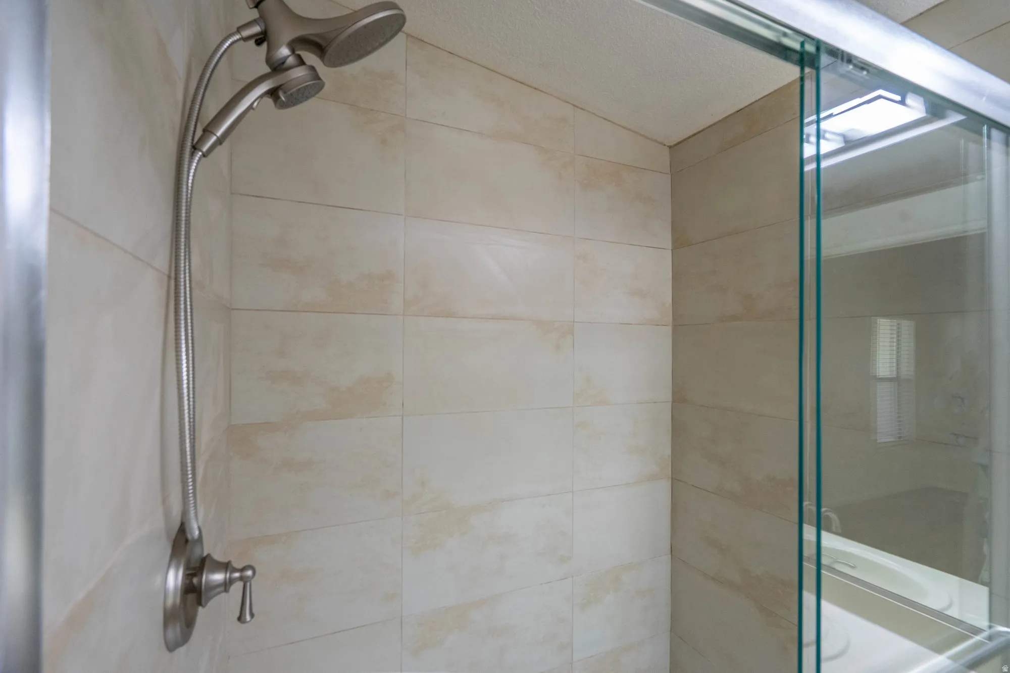 Shower enclosure featuring light-toned tile walls, brushed nickel fixtures, a dual shower head, and a clear glass sliding door