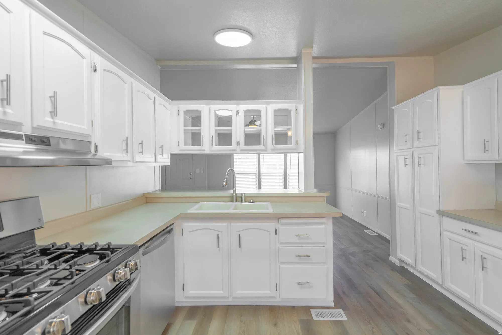 Kitchen featuring white cabinetry, light countertops, wood-finish flooring, a stainless steel range, and a built-in sink