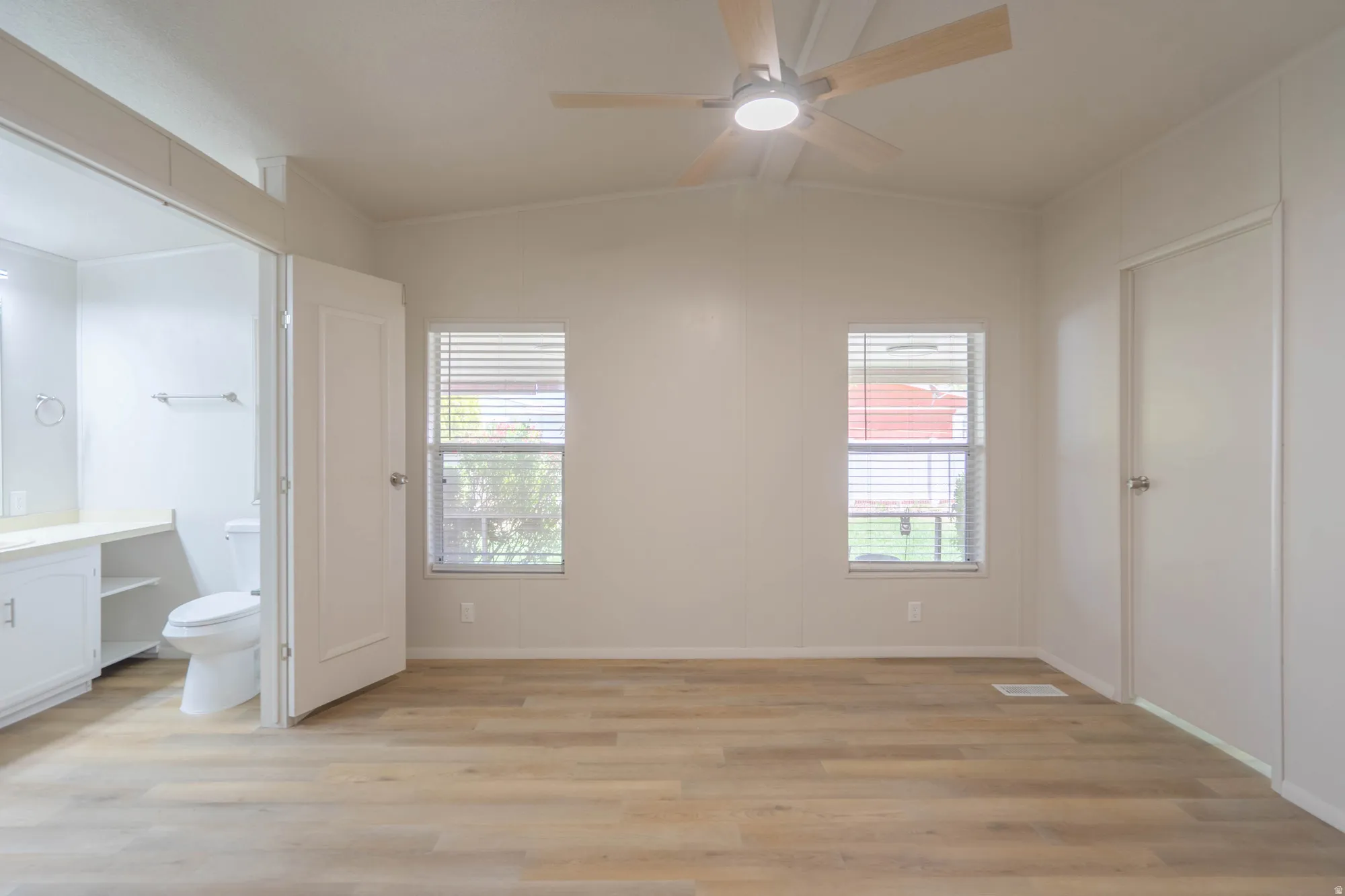 Spacious room featuring wood-finish flooring, two windows with blinds, and a ceiling fan