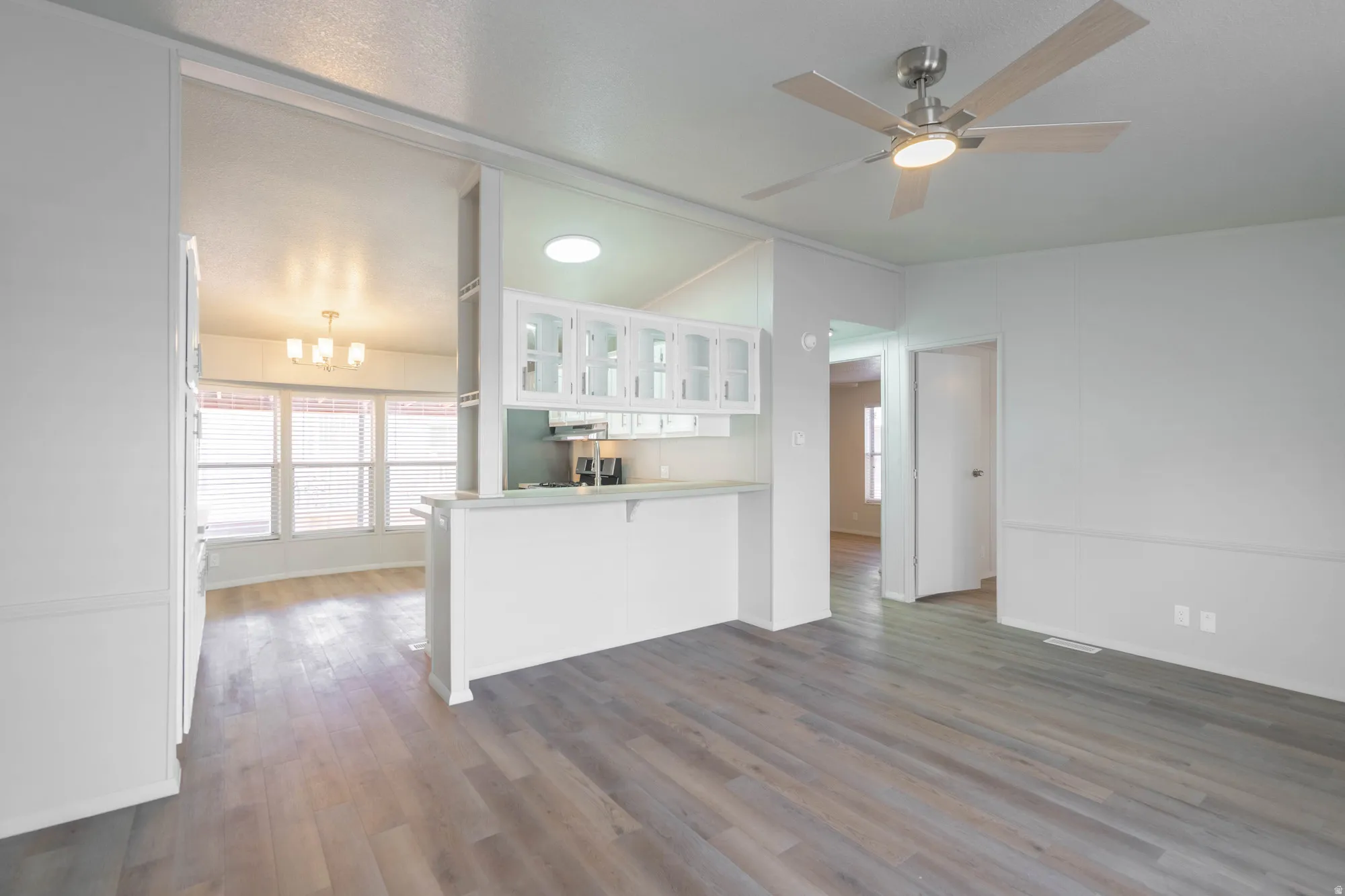 Open-concept living space featuring wood-finish flooring, a ceiling fan with integrated lighting, and white wainscoting