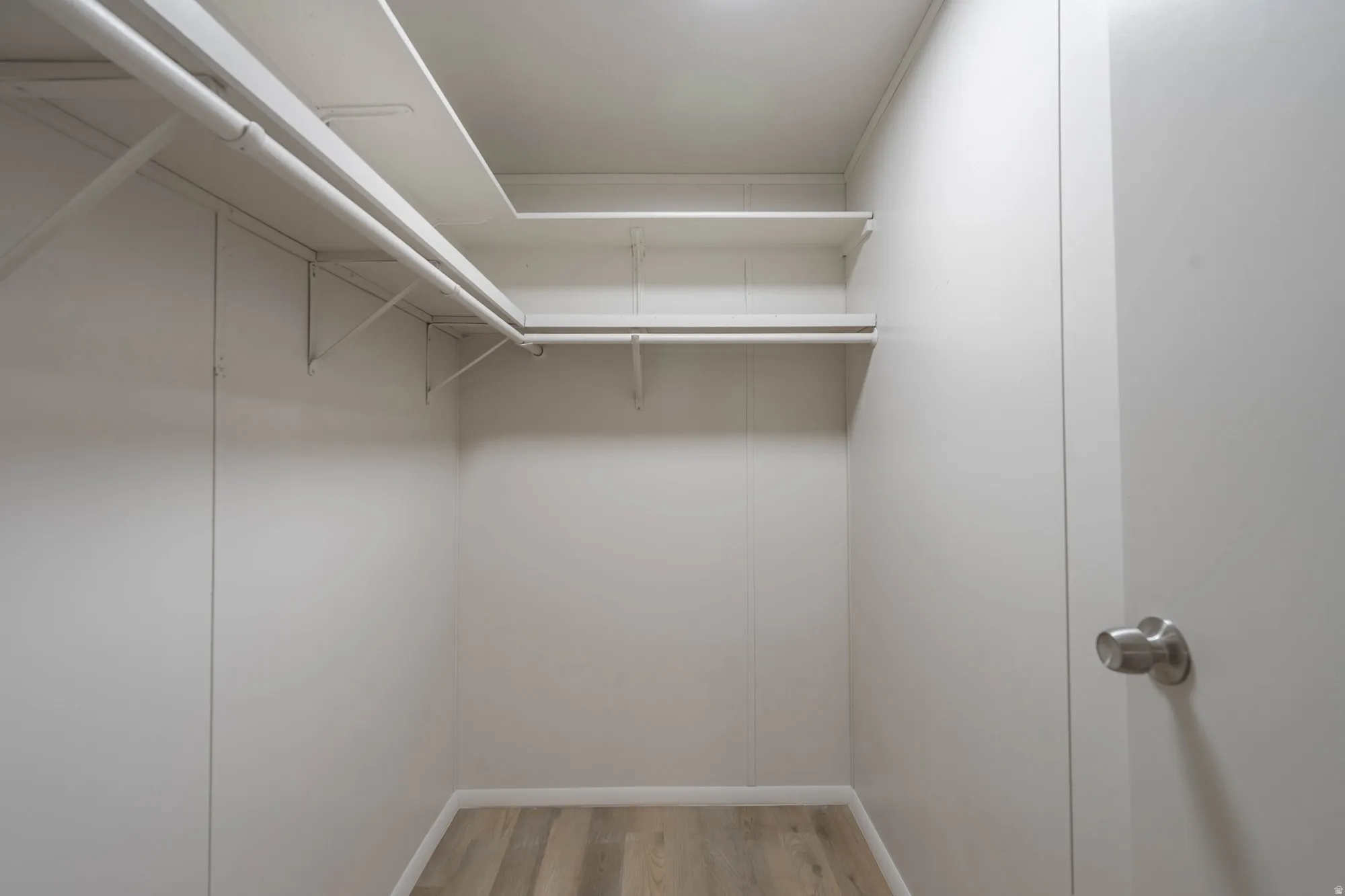 Walk-in closet featuring light wood-finish flooring, white walls, and built-in shelving with hanging rods
