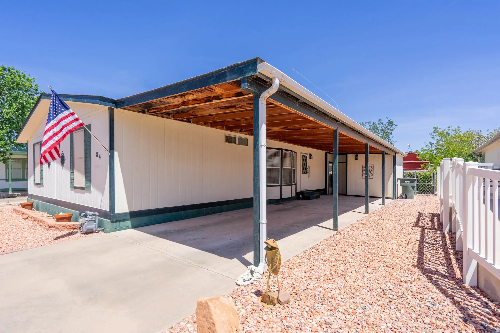 Exterior featuring a covered concrete carport, white siding, dark trim, and a white fence