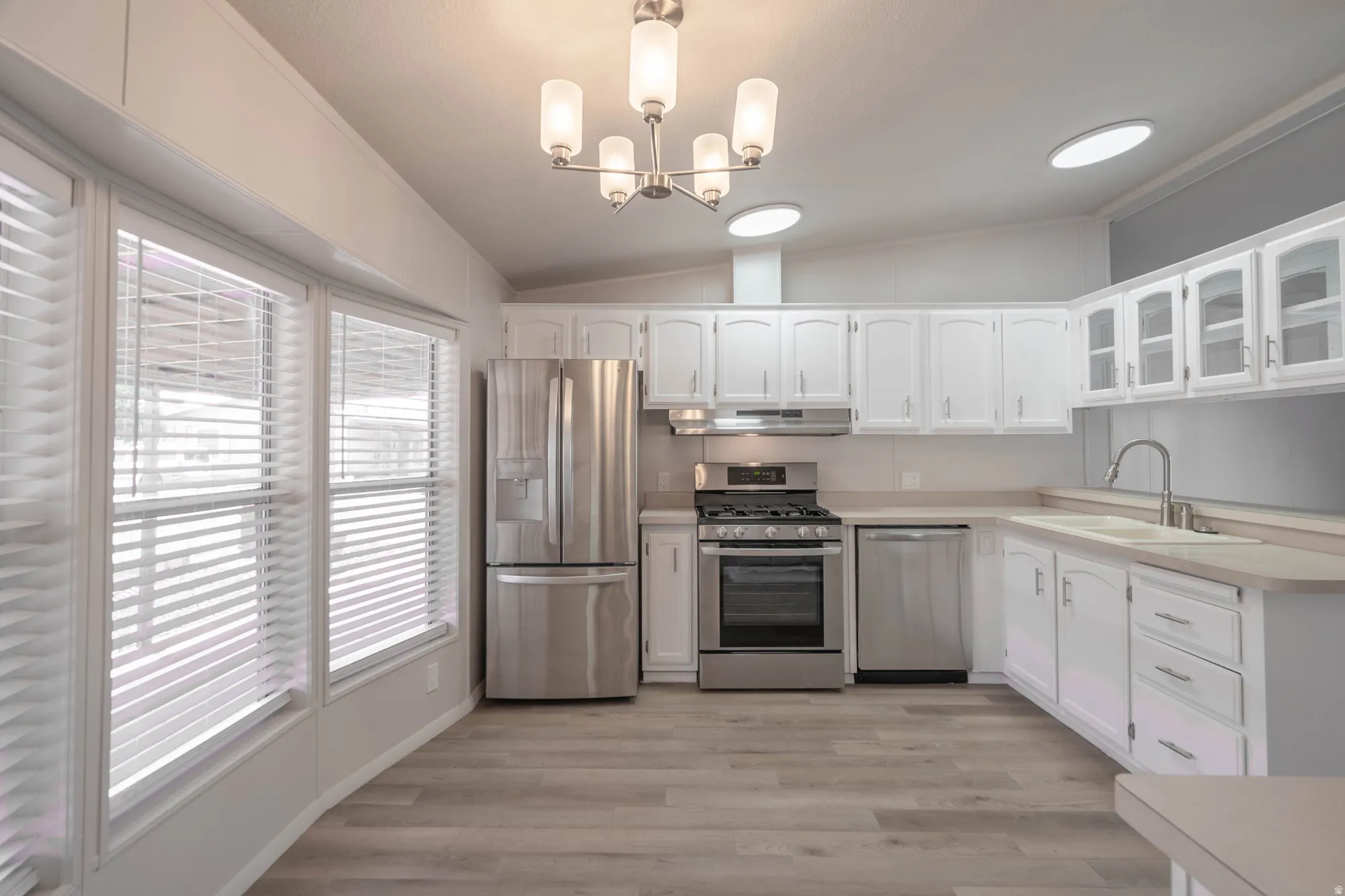 Modern kitchen featuring white cabinetry, stainless steel appliances, wood-finish flooring, and a contemporary chandelier
