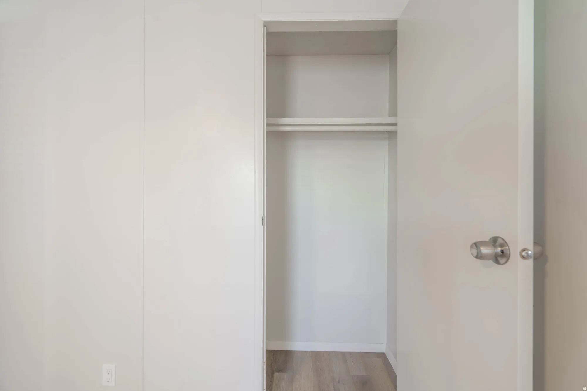 Recessed closet with a single hanging rod and upper shelf, featuring wood-finish flooring
