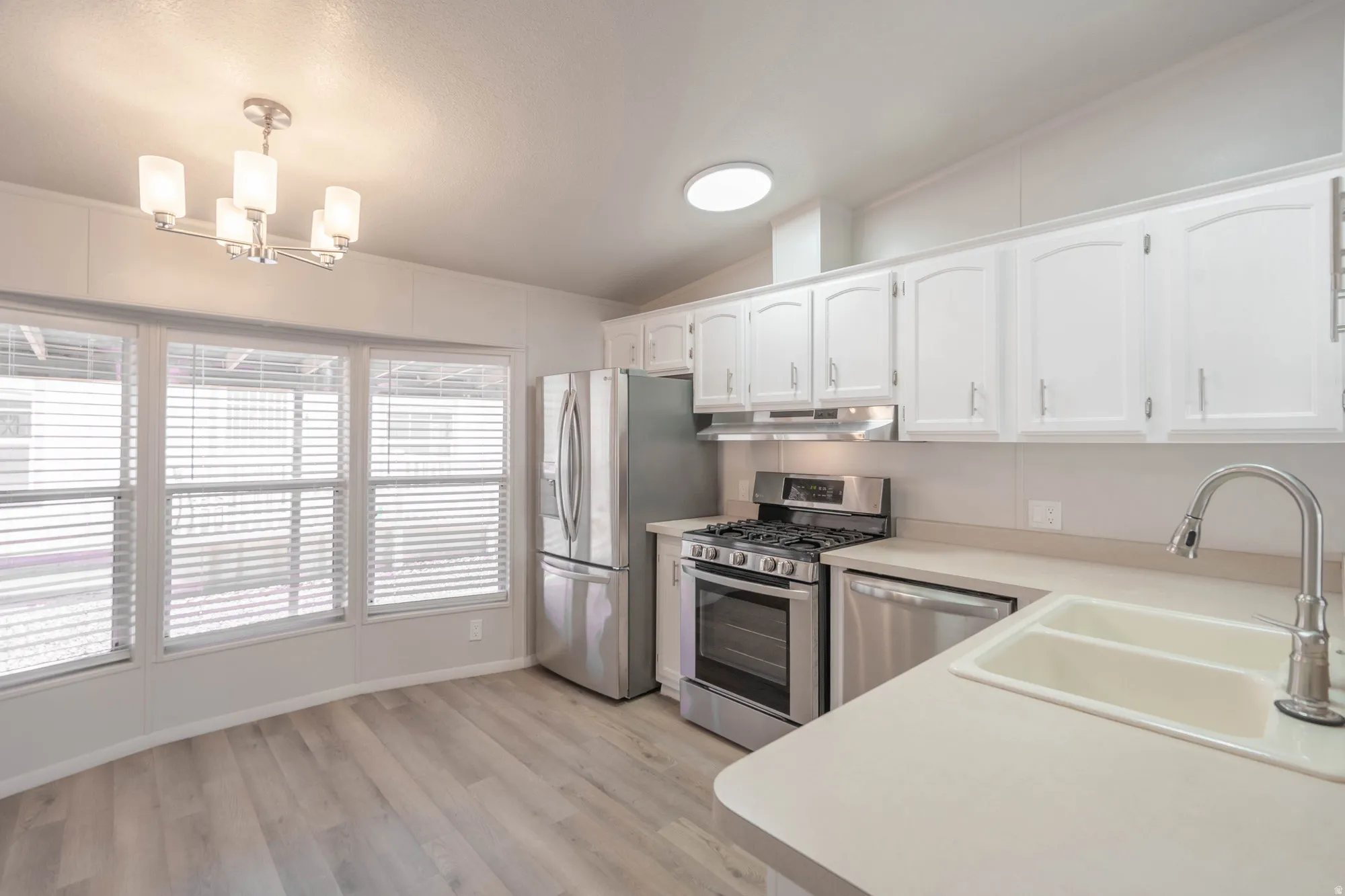Kitchen featuring wood-finish flooring, white cabinetry, stainless steel appliances, and a dual basin sink with a pull-down faucet