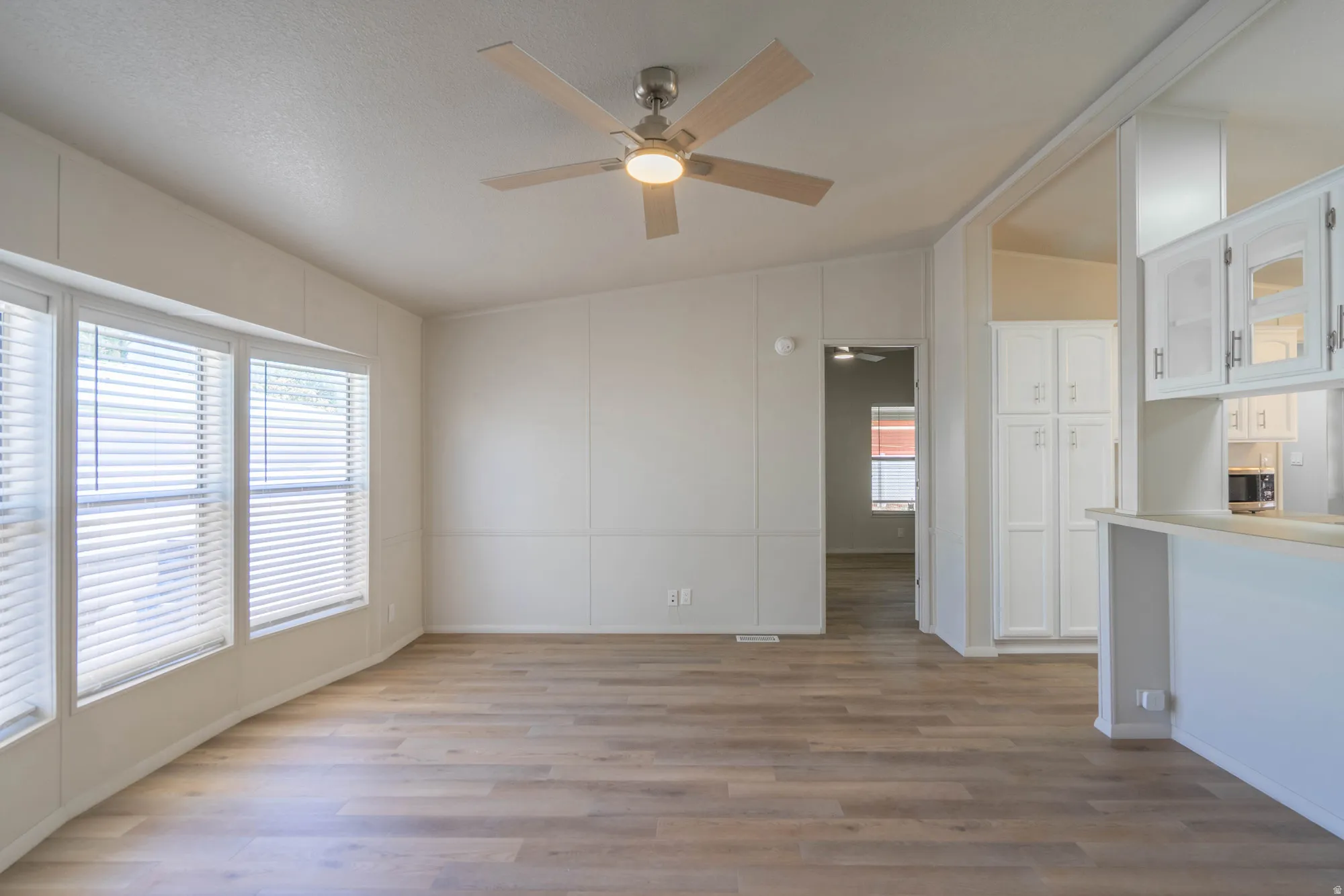 Open concept living area featuring wood-finish flooring, a ceiling fan with integrated lighting, and multiple windows with blinds
