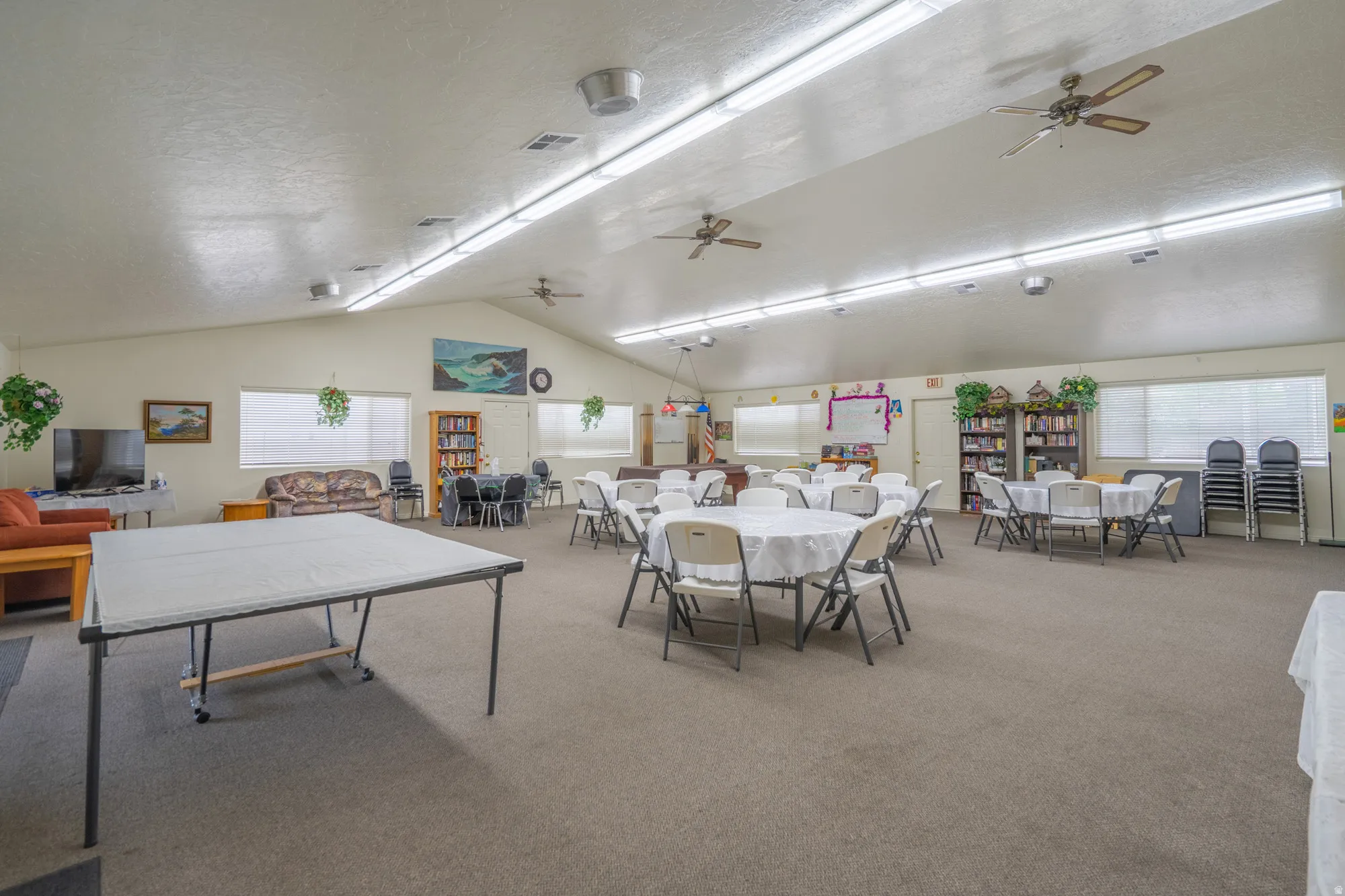 Spacious interior room featuring a vaulted ceiling with exposed beams, multiple ceiling fans, and recessed lighting fixtures