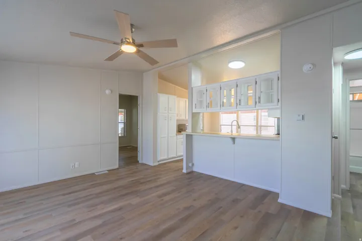 Open-concept living area featuring wood-finish flooring, a contemporary ceiling fan, and a pass-through kitchen counter with white cabinetry and built-in lighting