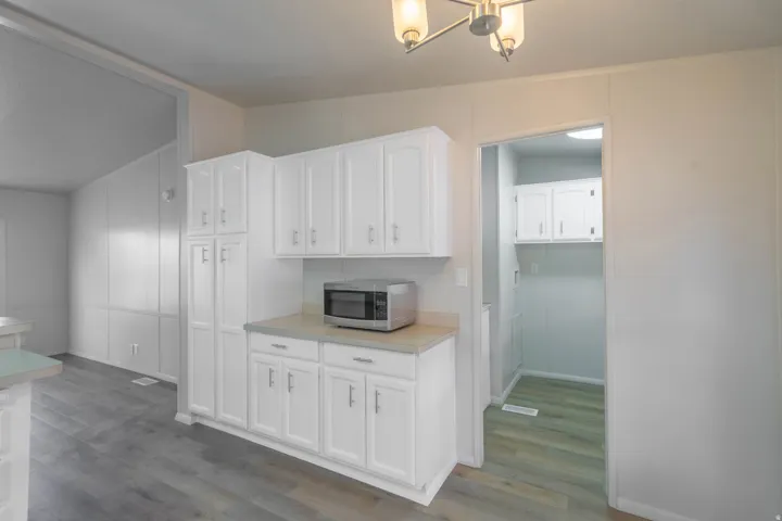 White cabinetry with brushed nickel hardware, laminate countertops, wood-finish flooring, and a recessed pantry