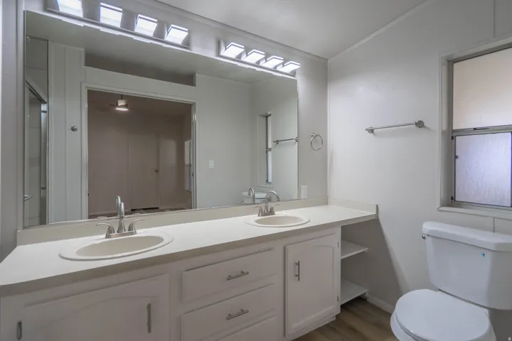 Bathroom featuring a dual vanity with white cabinetry and integrated sinks, a wide mirror, and vanity lighting