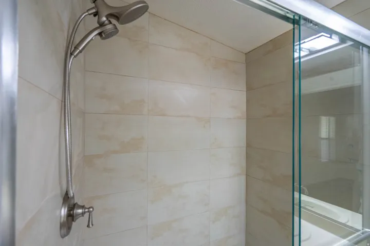 Shower enclosure featuring light-toned tile walls, brushed nickel fixtures, a dual shower head, and a clear glass sliding door