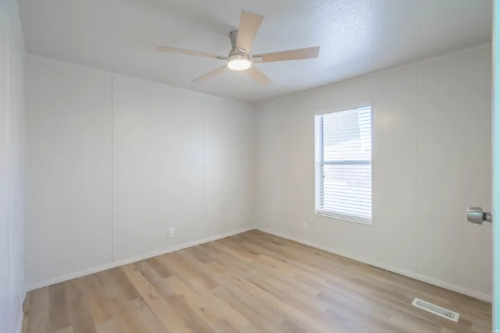 Light-filled room featuring wood-finish flooring, a contemporary ceiling fan with integrated lighting, a double-hung window with blinds, and white wall panels