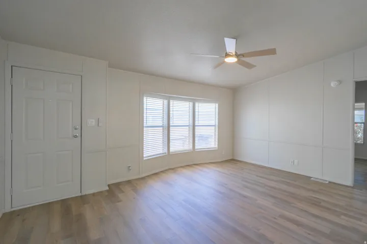 Bright living space featuring wood-finish flooring, a contemporary ceiling fan with integrated lighting, and multiple windows with horizontal blinds