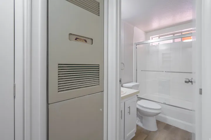 Bathroom with wood-finish flooring, white vanity cabinetry, white toilet, and a combination shower/tub with sliding glass enclosure